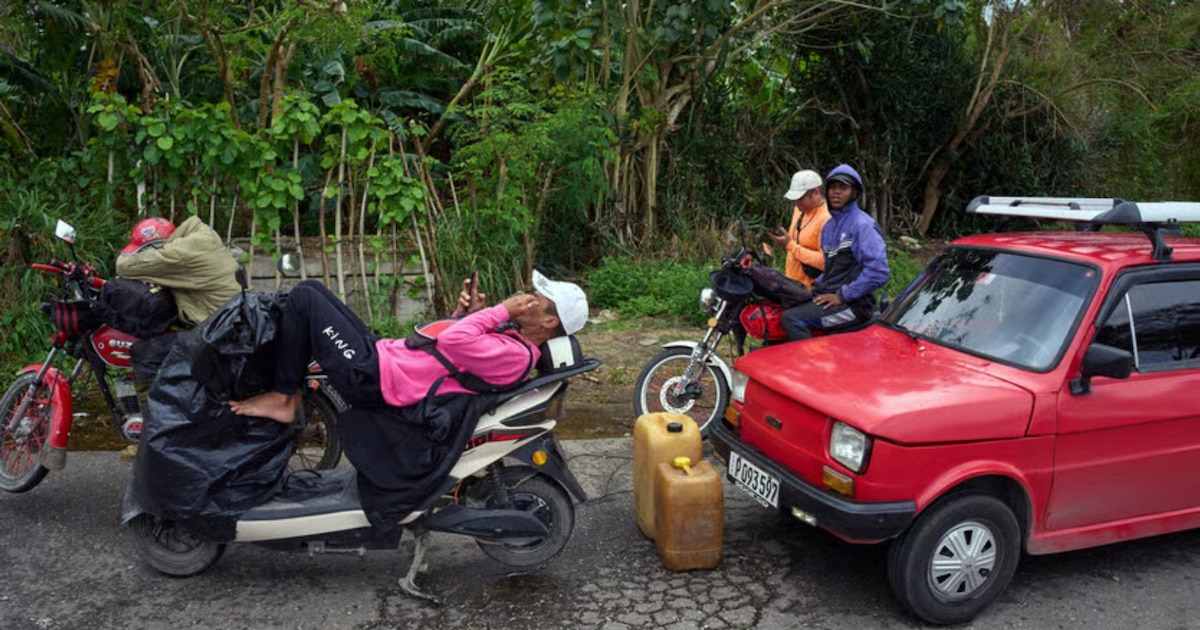 Fila de autos bajo el sol en Cuba esperando gasolina durante apagón de 16 horas con edificios oscuros al fondo