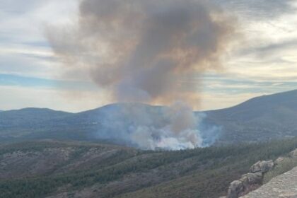 Bomberos forestales y helicóptero con cubeta de agua combatiendo el incendio en Acebo, Sierra de Gata, bajo cielo humeante