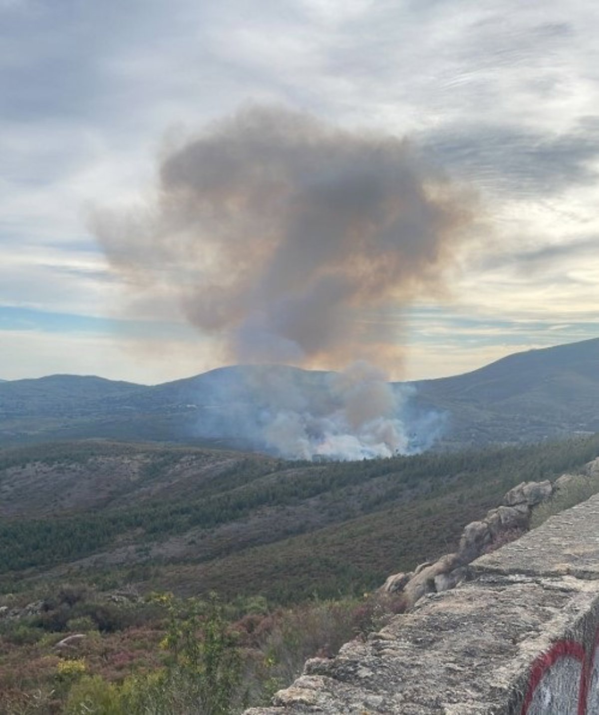 Bomberos forestales y helicóptero con cubeta de agua combatiendo el incendio en Acebo, Sierra de Gata, bajo cielo humeante