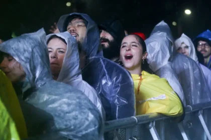 Multitud en el Estéreo Picnic bajo lluvia intensa en el Parque Simón Bolívar con artistas en escenario y asistentes con impermeables brillantes