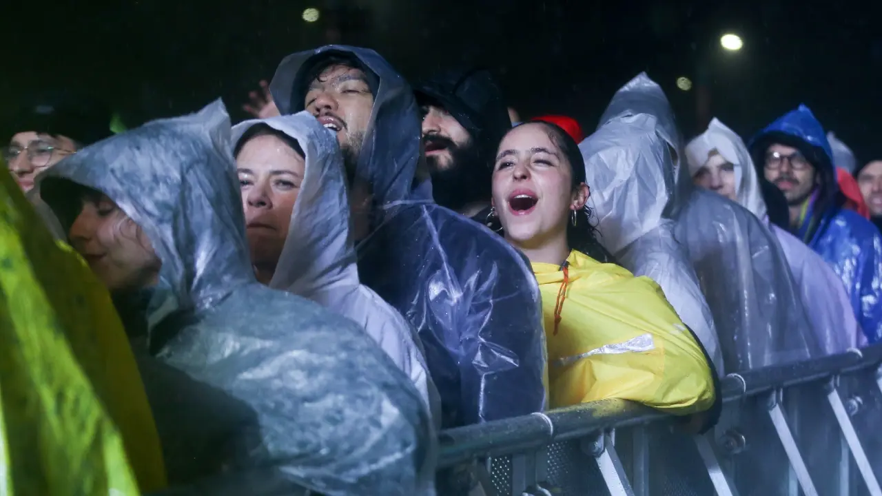 Multitud en el Estéreo Picnic bajo lluvia intensa en el Parque Simón Bolívar con artistas en escenario y asistentes con impermeables brillantes