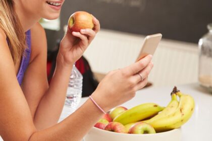 Persona comiendo con el móvil en la mano mientras la pantalla distrae su atención de un plato de comida saludable