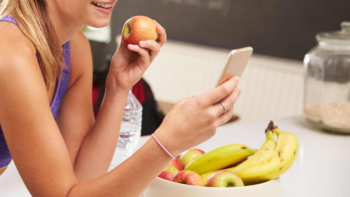 Persona comiendo con el móvil en la mano mientras la pantalla distrae su atención de un plato de comida saludable
