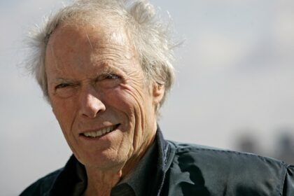 Clint Eastwood en una entrevista seria señalando con gesto crítico, rodeado de carteles de westerns clásicos como 'Unforgiven'