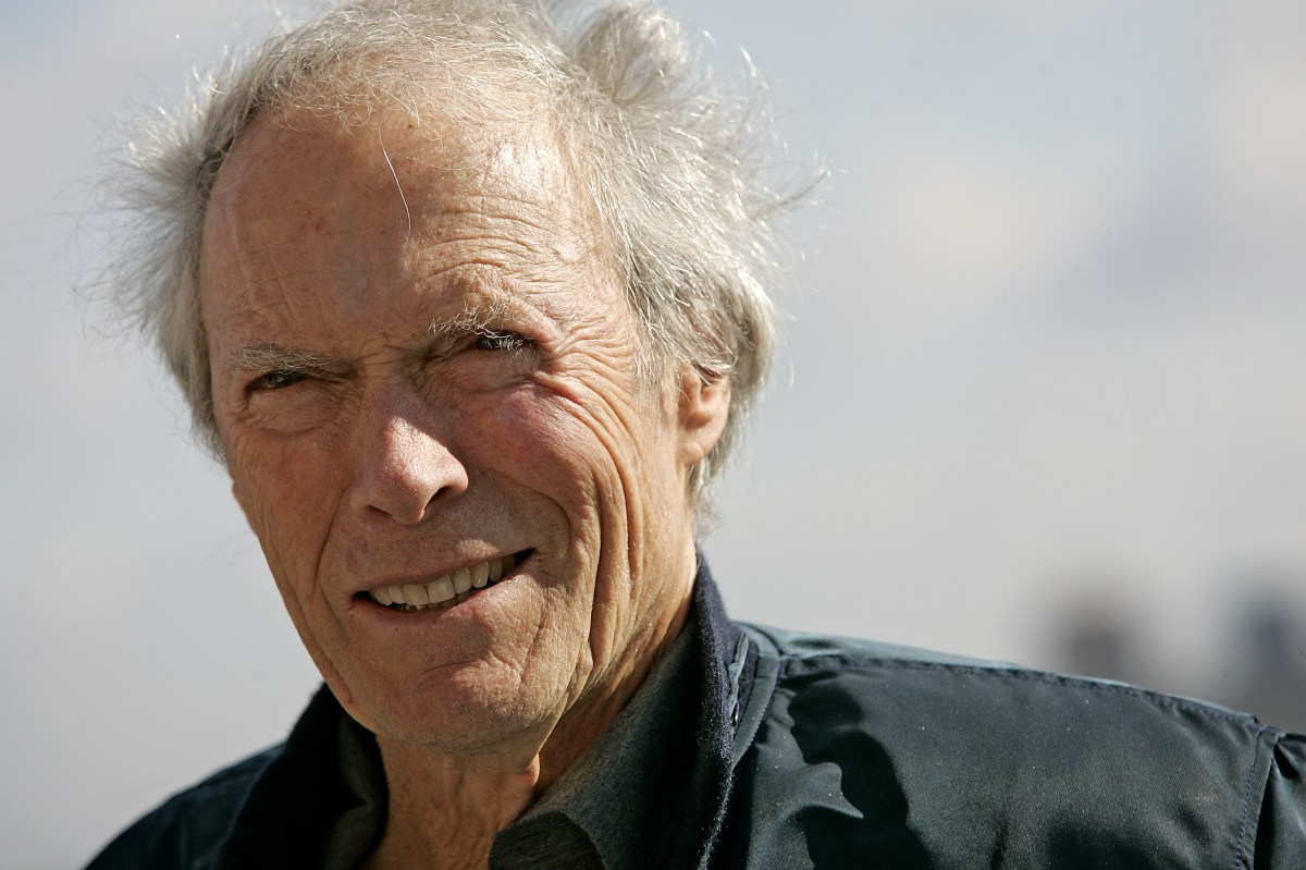 Clint Eastwood en una entrevista seria señalando con gesto crítico, rodeado de carteles de westerns clásicos como 'Unforgiven'