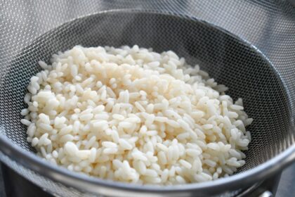 Arroz blanco con granos sueltos y textura al dente en un colador bajo chorro de agua fría, clave del método infalible