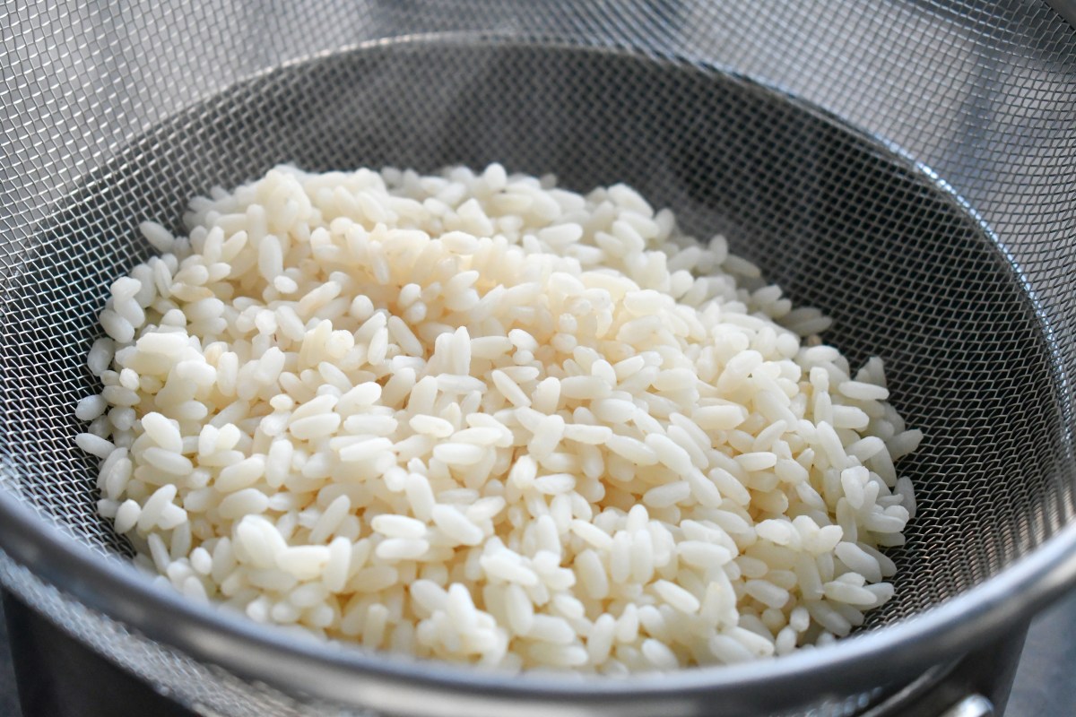 Arroz blanco con granos sueltos y textura al dente en un colador bajo chorro de agua fría, clave del método infalible
