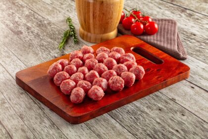 Albóndigas doradas y crujientes bañadas en salsa de tomate, con verduras frescas al fondo, mostrando el contraste de texturas del truco de enharinado