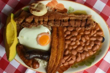 Bandeja paisa completa con arroz, frijoles, chicharrón, huevo, plátano, aguacate y arepa sobre mesa rústica, símbolo de la gastronomía colombiana que mezcla tradición y controversia