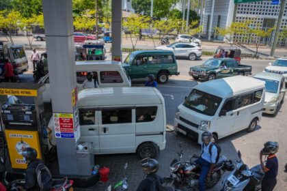 Barco petrolero en el Estrecho de Ormuz con humo de ataques al fondo mientras grúas portuarias detienen operaciones por crisis energética