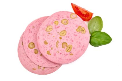 Embutido casero rosado cortado en lonchas sobre tabla de madera con zanahoria y remolacha fresca al fondo, rico en colágeno natural