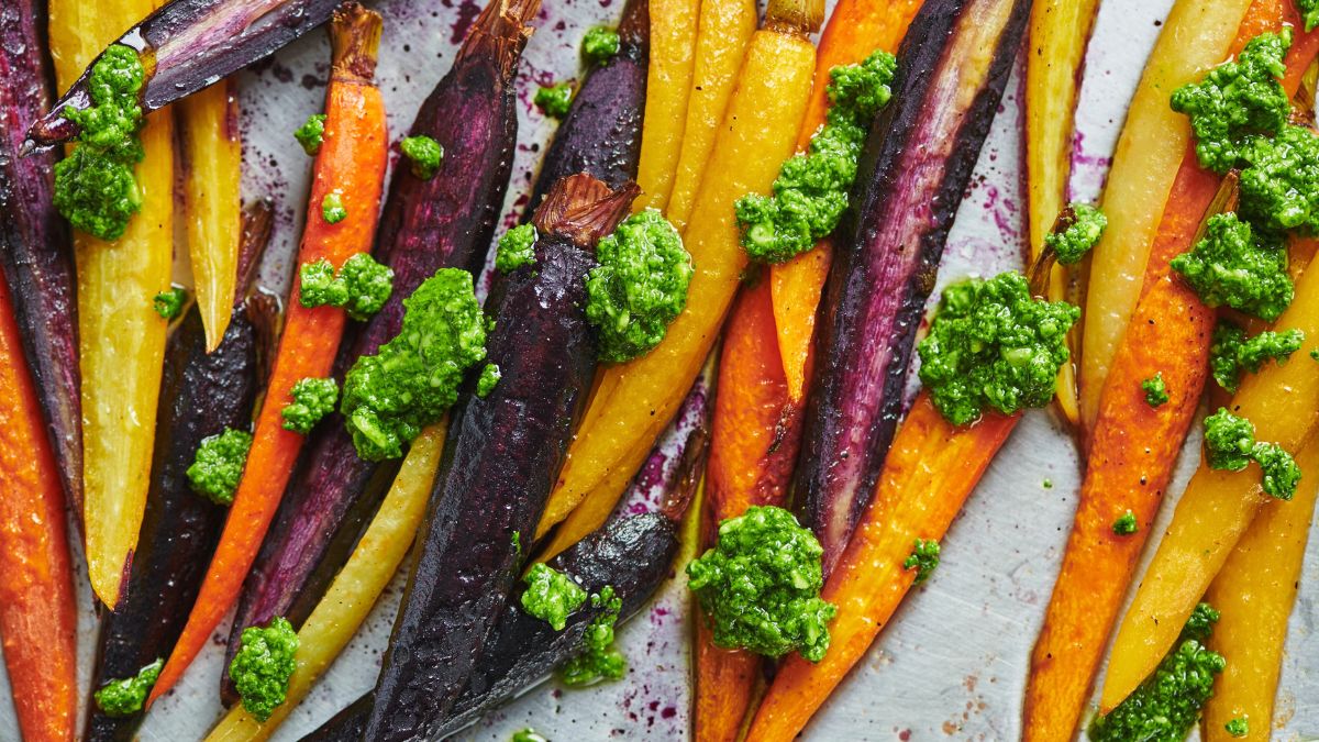 Zanahorias multicolor asadas al horno con bordes caramelizados y pesto verde fresco, lista para servir en mesa pascual