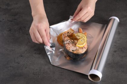 Rollos de papel aluminio reluciente junto a un cepillo y jabón sobre una encimera limpia, listos para su lavado y reutilización segura