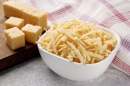 Paquete de queso cheddar crudo con etiqueta de retiro por riesgo de E. coli junto a lista de lotes afectados