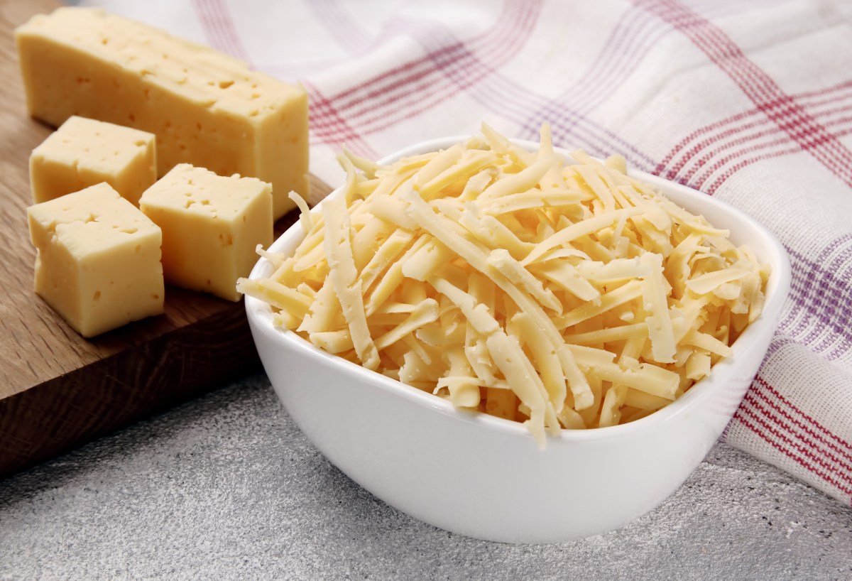 Paquete de queso cheddar crudo con etiqueta de retiro por riesgo de E. coli junto a lista de lotes afectados