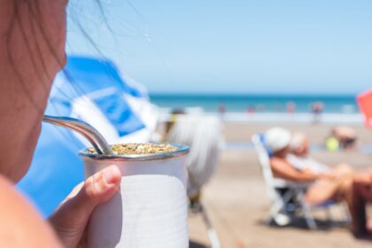 Latas de yerba mate SOLLOS en sabores piña y coco sobre tabla de surf flotando en aguas turquesas, estilo costero 2026