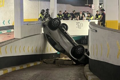 Coche volcado tras caer desde una rampa en el parking público de Olavide, con equipos de emergencia trabajando en la zona