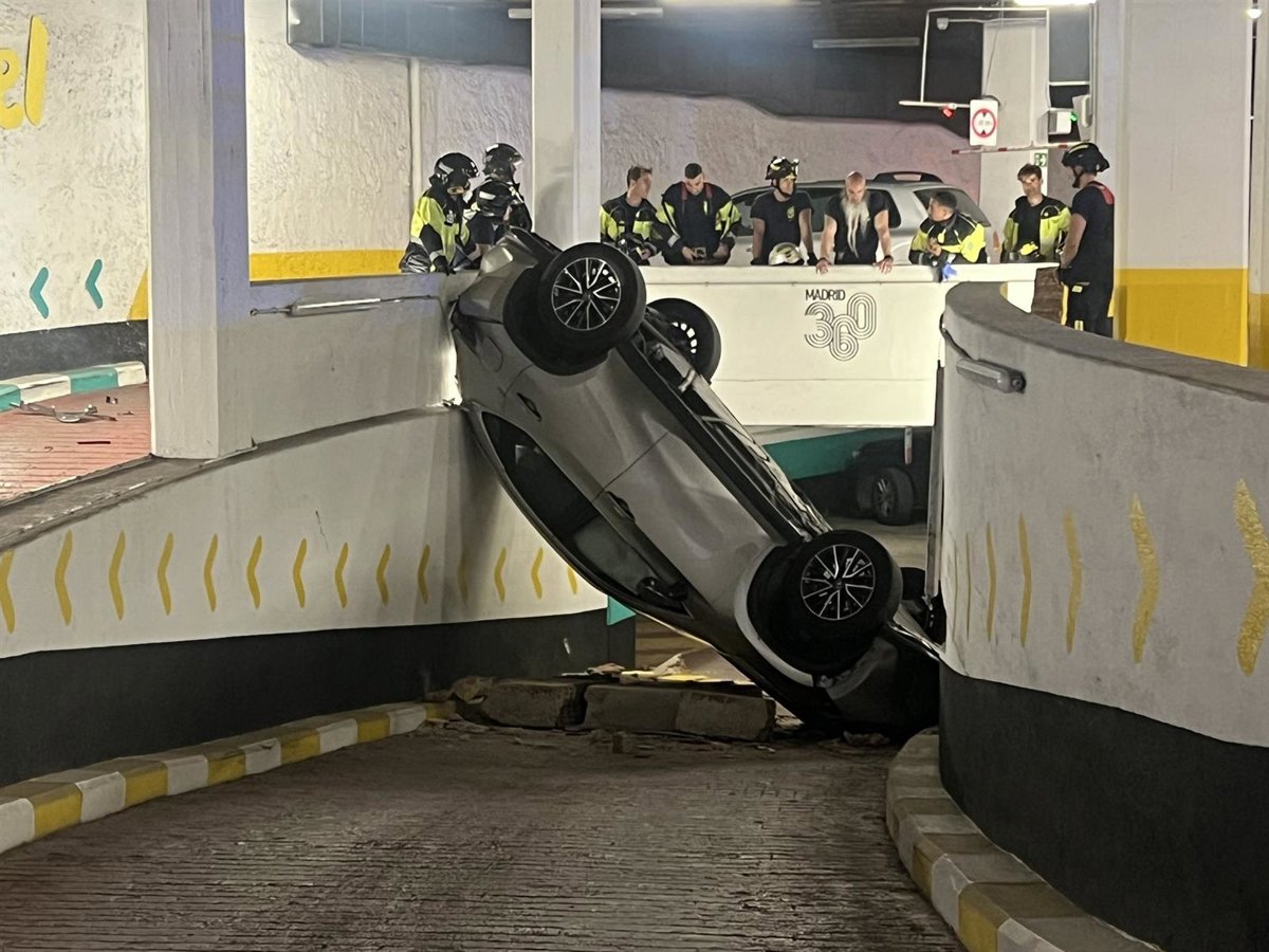 Coche volcado tras caer desde una rampa en el parking público de Olavide, con equipos de emergencia trabajando en la zona