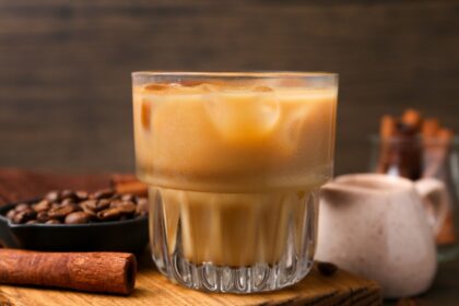 Taza humeante con infusión dorada de clavo y canela, rodeada de especias enteras sobre mesa de madera