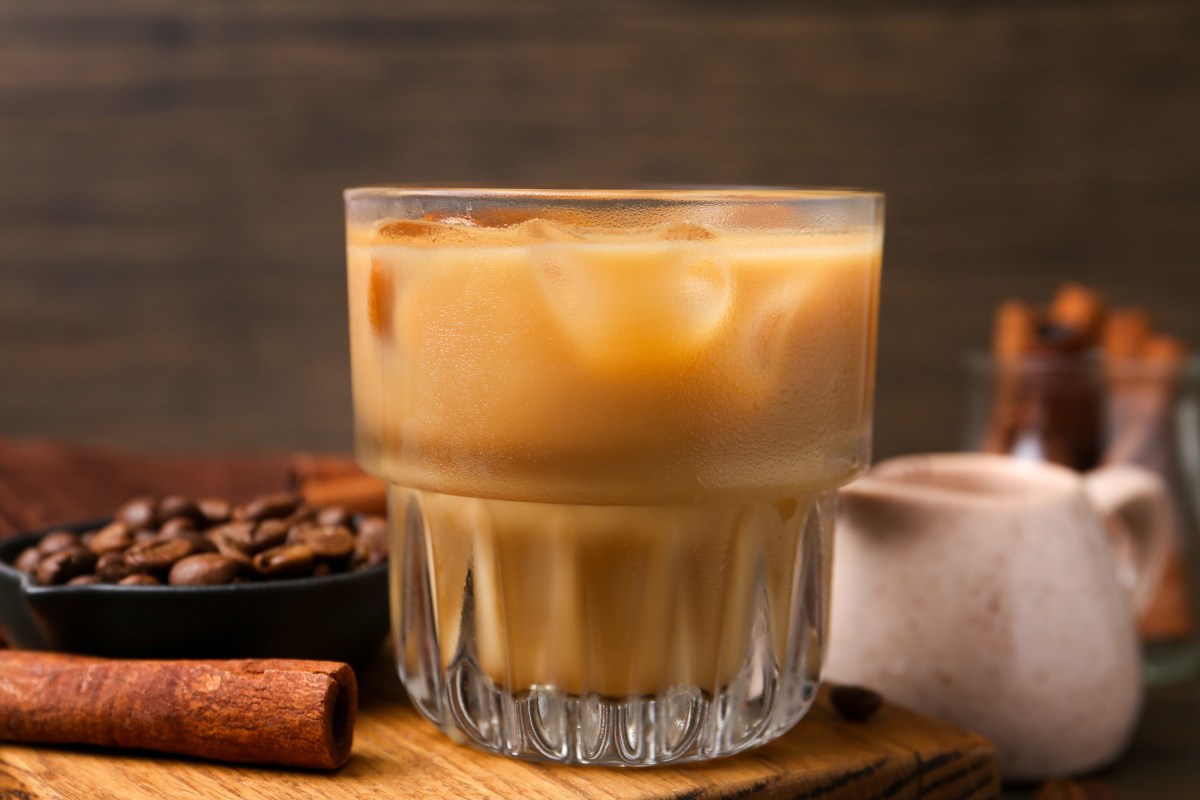 Taza humeante con infusión dorada de clavo y canela, rodeada de especias enteras sobre mesa de madera