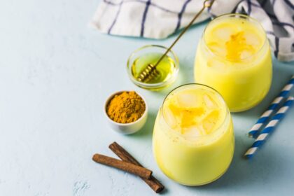 Vaso de golden milk con especias flotantes: cúrcuma, canela y pimienta negra sobre fondo dorado, lista para proteger tu hígado