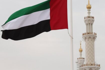Bandera de los EAU ondeando frente a un gráfico de barriles de petróleo con flechas en direcciones opuestas, simbolizando la ruptura con la OPEP