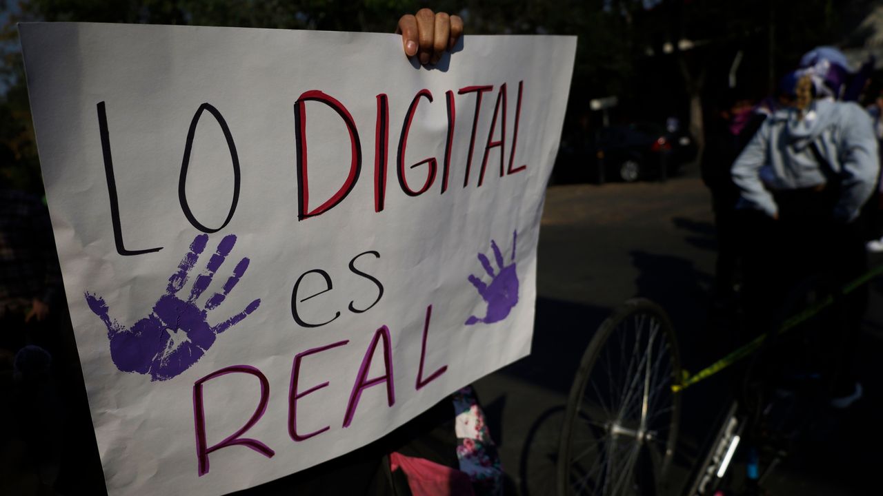 Mano femenina sosteniendo un celular con pantalla rota y la leyenda 'Ley Olimpia: 5 años de impunidad' sobre un fondo de expedientes judiciales apilados