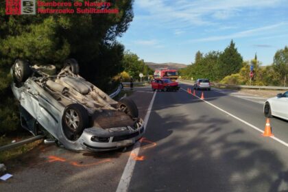 Vehículo volcado tras colisión lateral en carretera secundaria con señalización horizontal y falta de barreras de contención