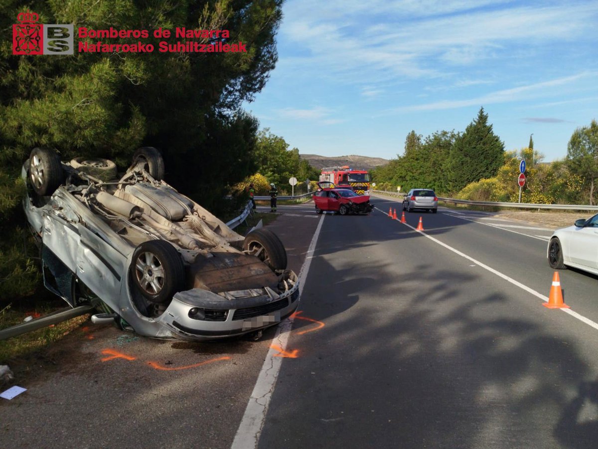 Vehículo volcado tras colisión lateral en carretera secundaria con señalización horizontal y falta de barreras de contención