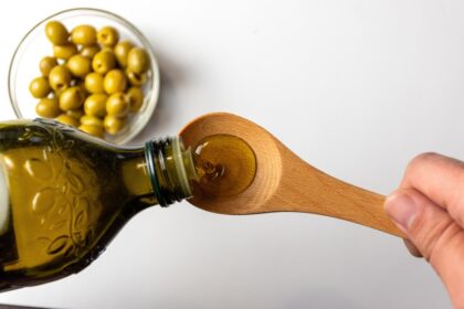 Frasco de AOEV dorado con aceitunas verdes y gráfico de bacterias intestinales Adlercreutzia resaltando su conexión cerebro-intestino
