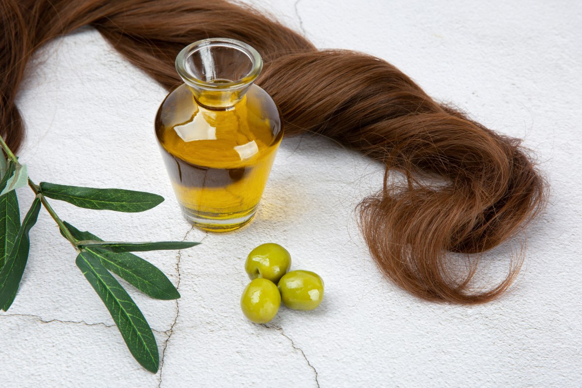 Frasco de aceite de oliva virgen extra junto a un cepillo con hebras de cabello saludable, destacando su uso contra la alopecia
