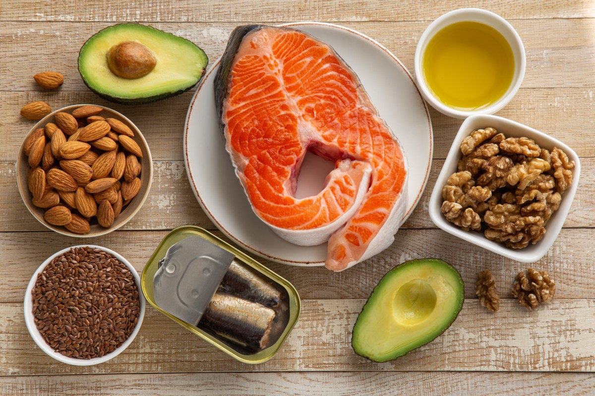 Variedad de alimentos ricos en grasas saludables: aguacate, aceite de oliva, salmón y huevos con yema brillante sobre mesa rústica