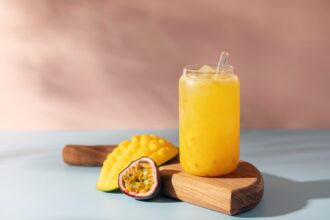Vaso transparente con agua de mango y maracuyá mostrando capas vibrantes: pulpa amarilla sobre hielo y cubos de mango Ataulfo en el fondo, textura sedosa sin grumos