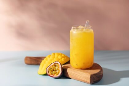Vaso transparente con agua de mango y maracuyá mostrando capas vibrantes: pulpa amarilla sobre hielo y cubos de mango Ataulfo en el fondo, textura sedosa sin grumos