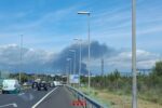Bomberos trabajando en el incendio de una nave logística con humo denso y vehículos en el interior