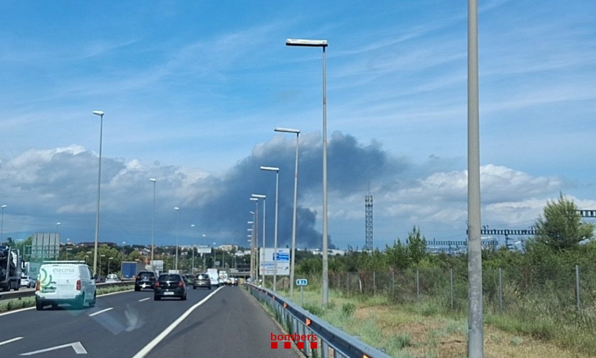 Bomberos trabajando en el incendio de una nave logística con humo denso y vehículos en el interior