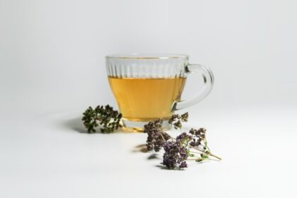 Taza de té de orégano con hojas frescas y secas sobre mesa de madera